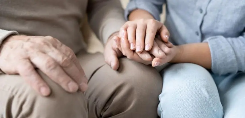 En äldre mans och kvinnas händer på varandra på hans knä.