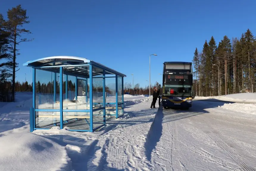 Busskur i snö. person på väg in i en blå dubbeldäckare.