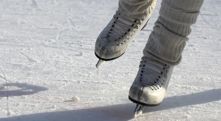 Två ben med konståkningsskridskor och benvärmare på frostig is.