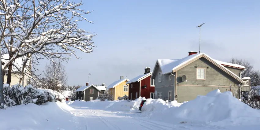 Olikfärgade hus utefter snöig gata.