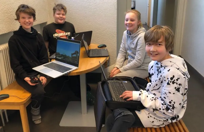 Fyra elever sitter med laptops och ler mot kameran. En visar upp skärm med Minecraft.